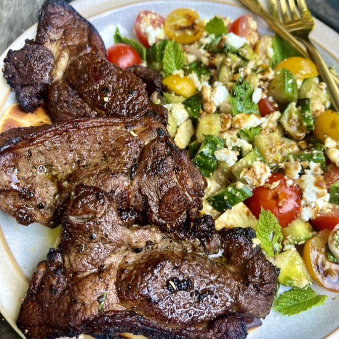 Lamb steaks with a feta salad on a white plate.